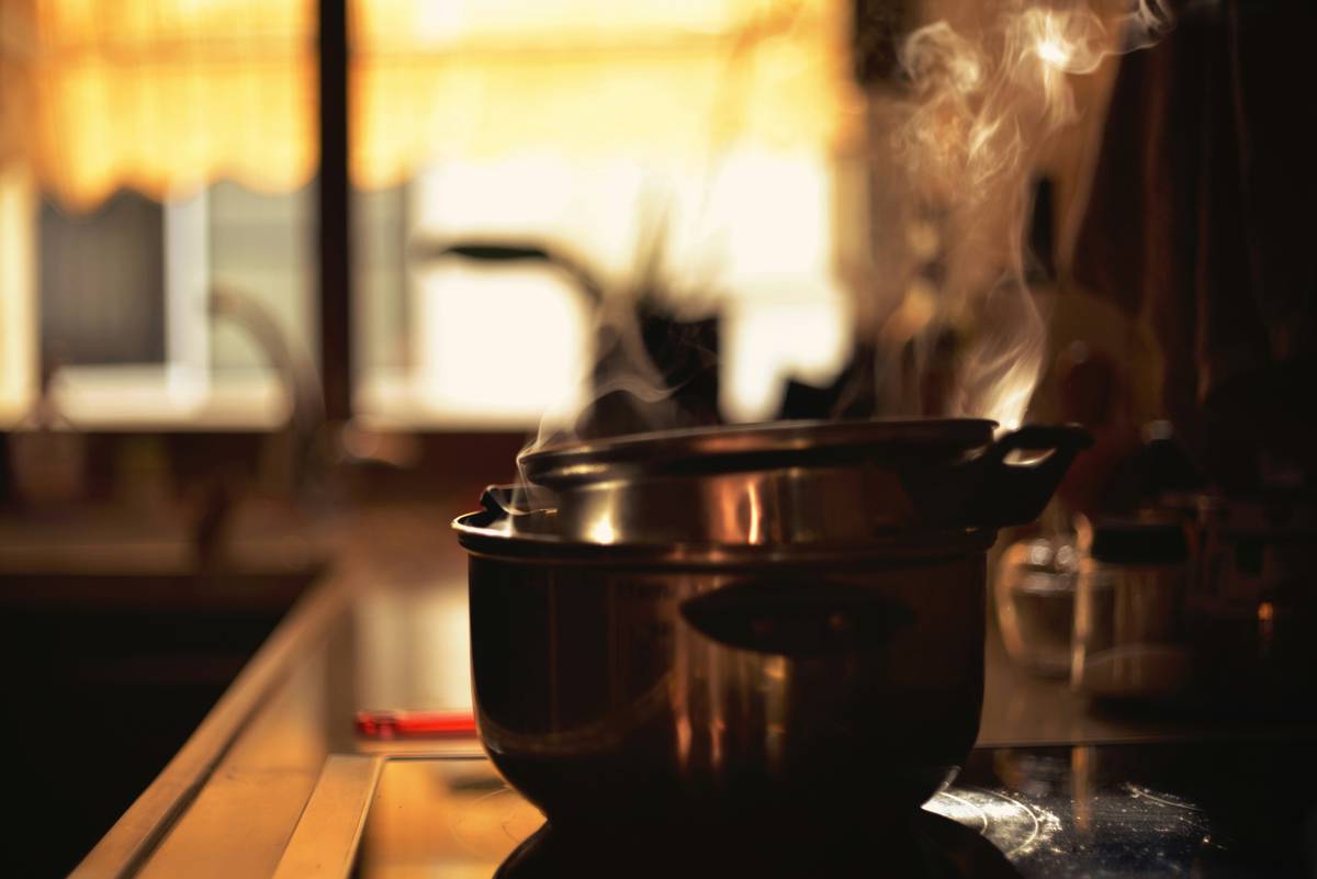 Close-up photo of a disassembled stovetop pressure cooker showing the brass steam pressure safety valve mounted on the lid, with visible gasket and spring housing